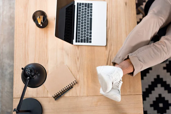 Top view of laptop with blank screen near male legs in white sneakers on table — Stock Photo