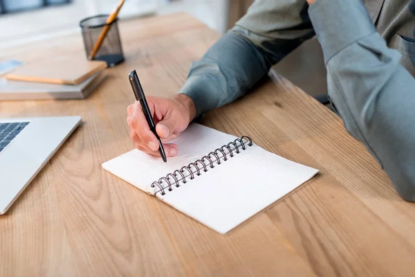 Visão cortada de homem de negócios escrevendo em notebook no escritório moderno — Fotografia de Stock