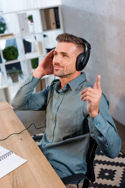 Feliz hombre de negocios escuchando música en auriculares en la oficina moderna - foto de stock