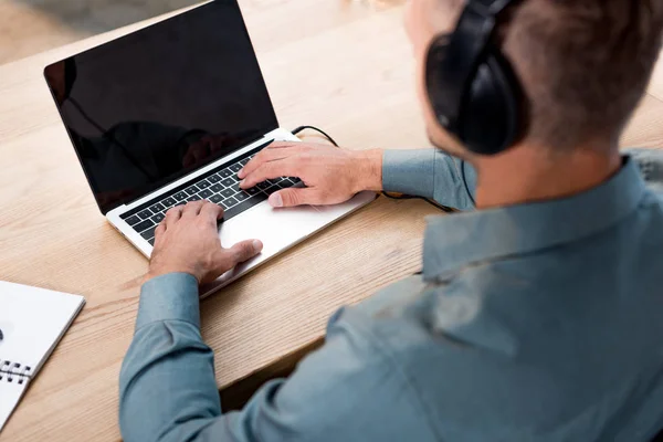 Selektiver Fokus des Mannes, der Musik über Kopfhörer hört, während er Laptop mit leerem Bildschirm benutzt — Stockfoto