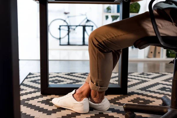 Обрезанный вид бизнесмена, сидящего в белых кроссовках в современном офисе — стоковое фото