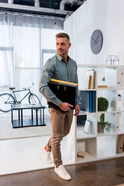 Щасливий бізнесмен, що стоїть з папками в сучасному офісі — стокове фото