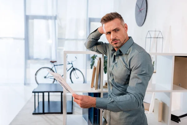Красивий чоловік стоїть і тримає газету в сучасному офісі — стокове фото