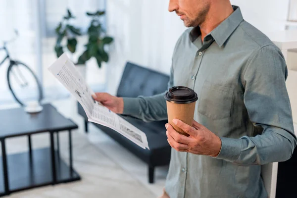 Vue recadrée d'un homme d'affaires lisant un journal et tenant une tasse en papier — Photo de stock