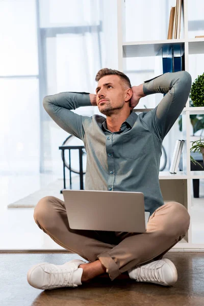 Nachdenklicher Geschäftsmann sitzt mit gekreuzten Beinen und Laptop auf dem Boden — Stockfoto