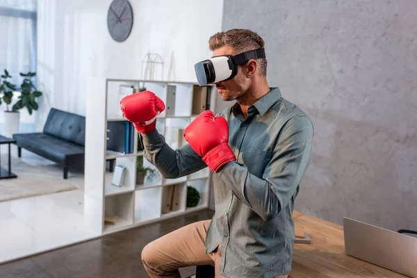 Businessman wearing virtual reality headset and boxing gloves in office — Stock Photo