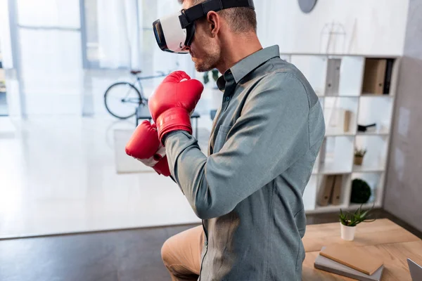 Confident businessman wearing virtual reality headset and boxing gloves in office — Stock Photo