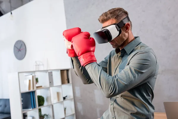 Serious businessman wearing virtual reality headset and boxing gloves in office — Stock Photo