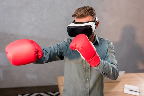 Selective focus of businessman wearing virtual reality headset and boxing gloves in office — Stock Photo