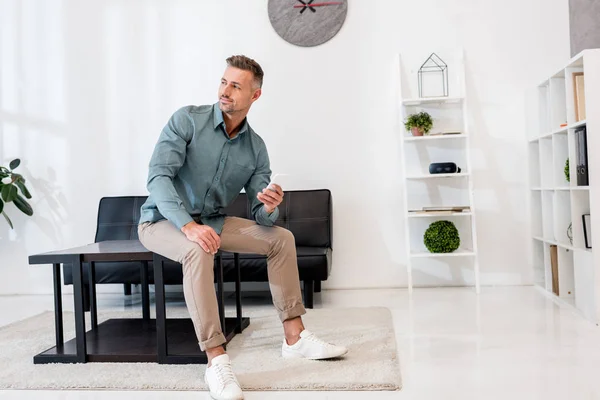 Handsome businessman sitting on coffee table and using smartphone — Stock Photo