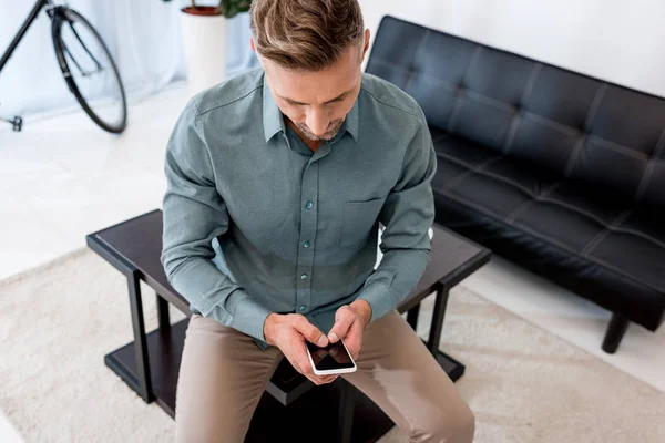 Overhead view of businessman sitting on coffee table and using smartphone with blank screen — Stock Photo