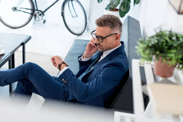 Bell'uomo d'affari in occhiali che guarda l'orologio mentre parla su smartphone — Foto stock