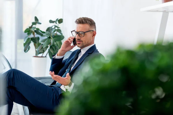 Вибірковий фокус серйозного бізнесмена в окулярах, що розмовляють на смартфоні — стокове фото