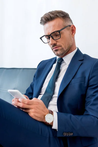 Bel homme d'affaires en lunettes et costume à l'aide d'un smartphone — Photo de stock