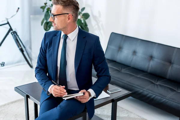 Schöner Geschäftsmann in Anzug und Brille mit Notizbuch und Stift — Stockfoto