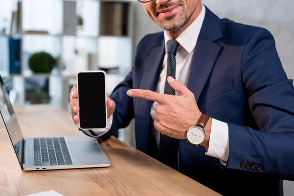 Ausgeschnittene Ansicht eines fröhlichen Geschäftsmannes, der mit dem Finger auf ein Smartphone mit leerem Bildschirm zeigt — Stockfoto