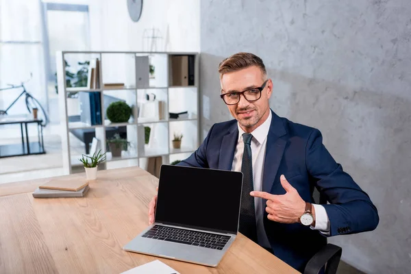 Empresário alegre apontando com o dedo para laptop com tela em branco — Fotografia de Stock