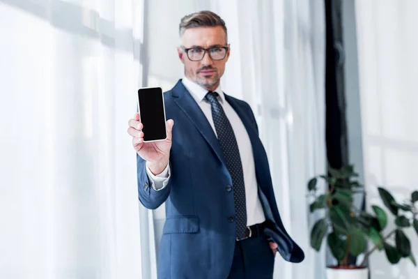 Enfoque selectivo de teléfono inteligente con pantalla en blanco en la mano de hombre de negocios guapo en traje - foto de stock