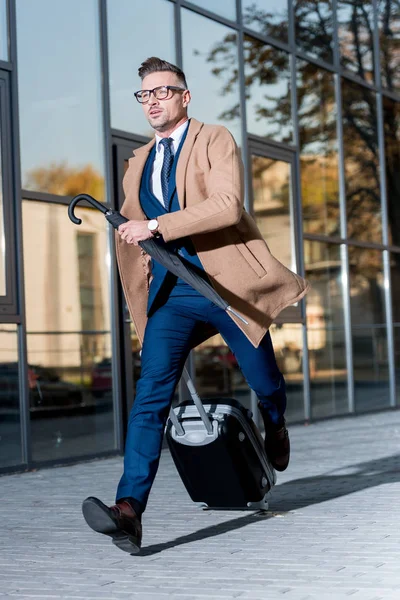 Guapo hombre de negocios corriendo con maleta y paraguas en la calle - foto de stock