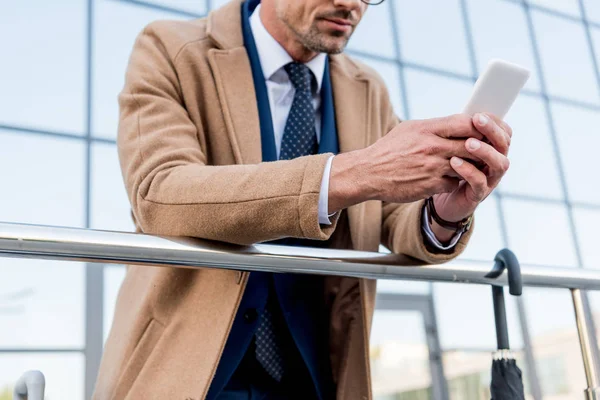 Cropped view of businessman using smartphone while standing in beige coat — Stock Photo