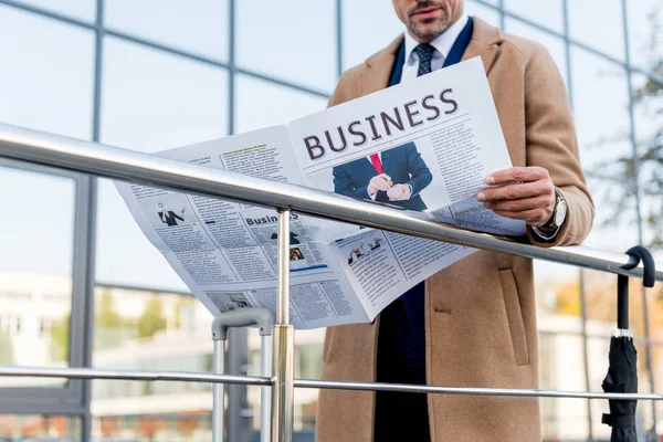 Vue recadrée d'un homme d'affaires debout en manteau beige et lisant un journal d'affaires — Photo de stock