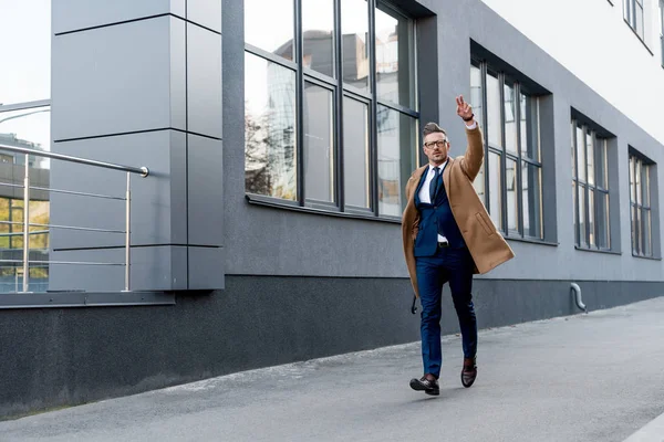 Hombre de negocios en abrigo beige mostrando señal de paz mientras corre por la calle - foto de stock