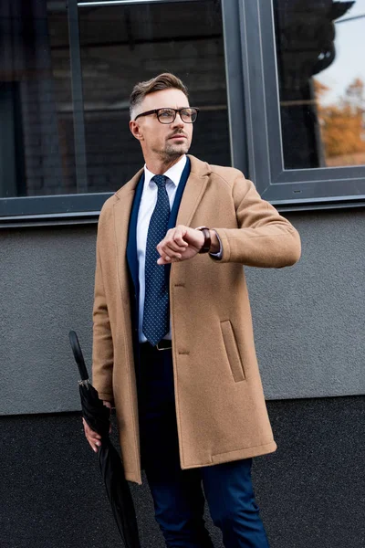 Schöner Geschäftsmann mit Armbanduhr in der Hand und Regenschirm in der Hand — Stockfoto