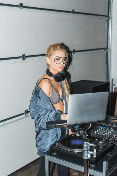 Atraente dj mulher em óculos e fones de ouvido olhando para laptop — Fotografia de Stock