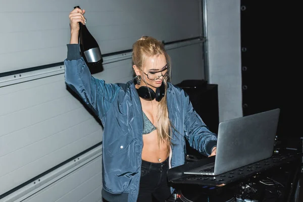 Alegre dj mulher segurando garrafa na mão e olhando para laptop — Fotografia de Stock