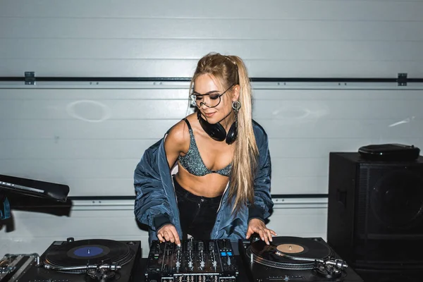 Atraente dj mulher em óculos de pé e olhando para discos de vinil — Fotografia de Stock