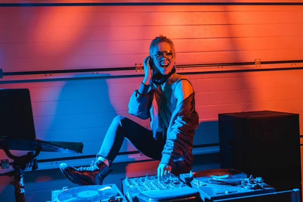 Cheerful dj girl in glasses touching dj mixer in nightclub — Stock Photo