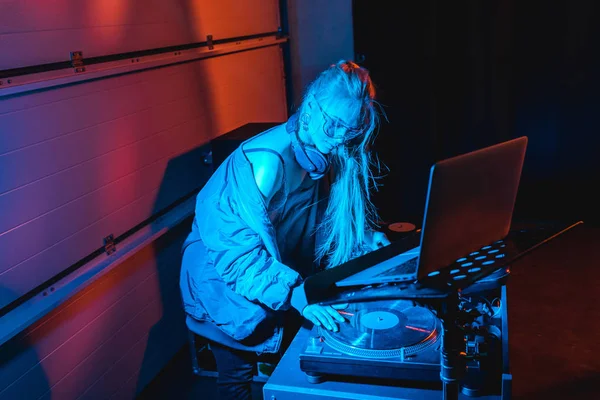 Fokussiertes DJ-Mädchen mit Brille berührt Schallplatte in der Nähe von Laptop in Nachtclub — Stockfoto