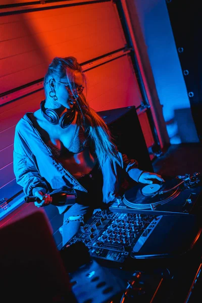 Blonde DJ-Frau hält Flasche, während sie Schallplatte berührt — Stockfoto