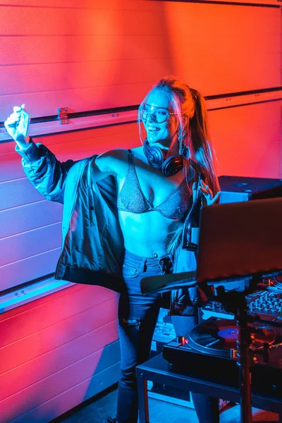 Cheerful blonde dj woman holding bottle and taking selfie in nightclub — Stock Photo