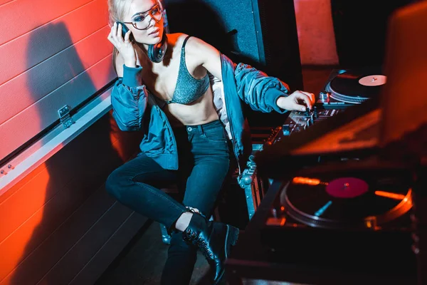Attraktives DJ-Mädchen mit blonden Haaren sitzt in der Nähe von DJ-Geräten und hört Musik über Kopfhörer — Stockfoto