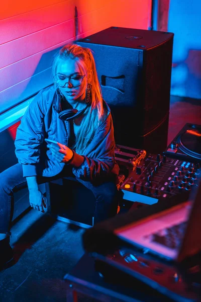 Привлекательная диджей-женщина с помощью смартфона, сидя в ночном клубе — стоковое фото