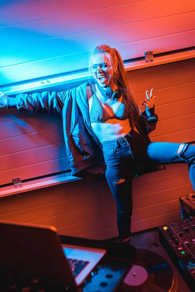 Избирательный фокус счастливой блондинки ди-джея в очках стоя и жестикулируя в ночном клубе — стоковое фото