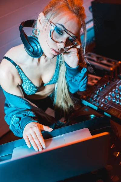 Rubia dj chica escuchar música en los auriculares y el uso de ordenador portátil en discoteca - foto de stock