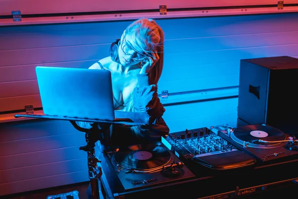 Bela loira dj mulher ouvindo música em fones de ouvido e usando laptop em boate — Fotografia de Stock