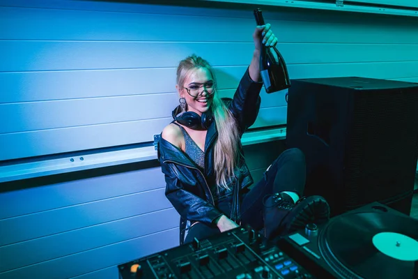 Alegre dj menina segurando garrafa com vinho na mão e sentado em boate — Fotografia de Stock