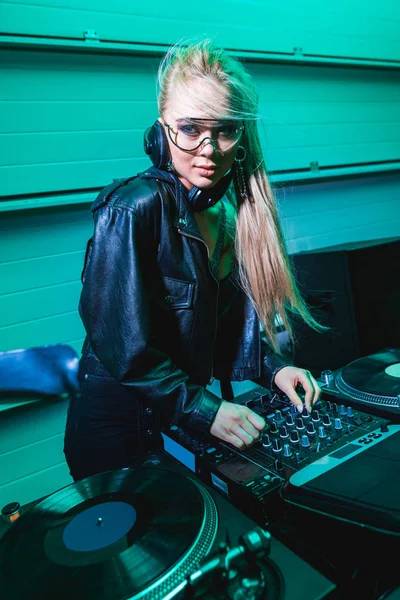 Blonde dj girl in glasses touching dj mixer in nightclub — Stock Photo