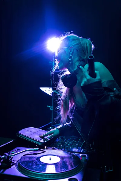 Cheerful and stylish dj woman holding bottle while touching dj equipment in nightclub — Stock Photo