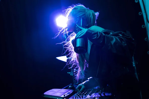 Blonde stilvolle DJ-Mädchen berühren dj Ausrüstung, während sie Flasche in einem Nachtclub halten — Stockfoto