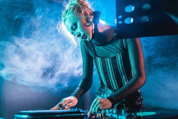 Selective focus of dj girl in headphones standing near dj mixer and touching vinyl record in nightclub with smoke — Stock Photo