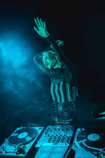 Blondes DJ-Mädchen hört Musik, während sie mit geschlossenen Augen in der Nähe von DJ-Geräten in einem Nachtclub mit Rauch steht — Stockfoto