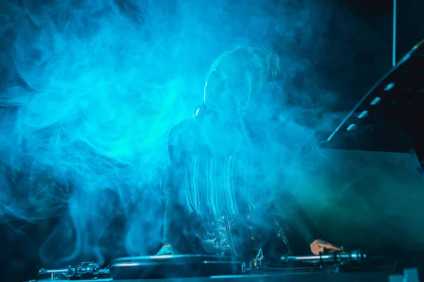 Dj girl using dj equipment in nightclub with smoke — Stock Photo