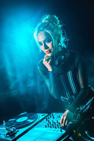 Hermosa rubia dj chica usando dj equipo en nightclub con humo — Stock Photo