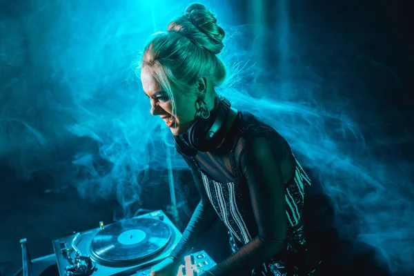 Angry blonde dj girl using dj equipment in nightclub with smoke — Stock Photo
