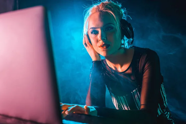 Mujer dj con cabello rubio escuchando música en los auriculares mientras usa el ordenador portátil - foto de stock