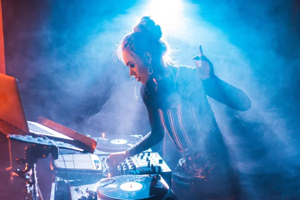 Concentré dj femme avec des cheveux blonds gestuelle et en utilisant l'équipement dj dans la boîte de nuit avec de la fumée — Photo de stock